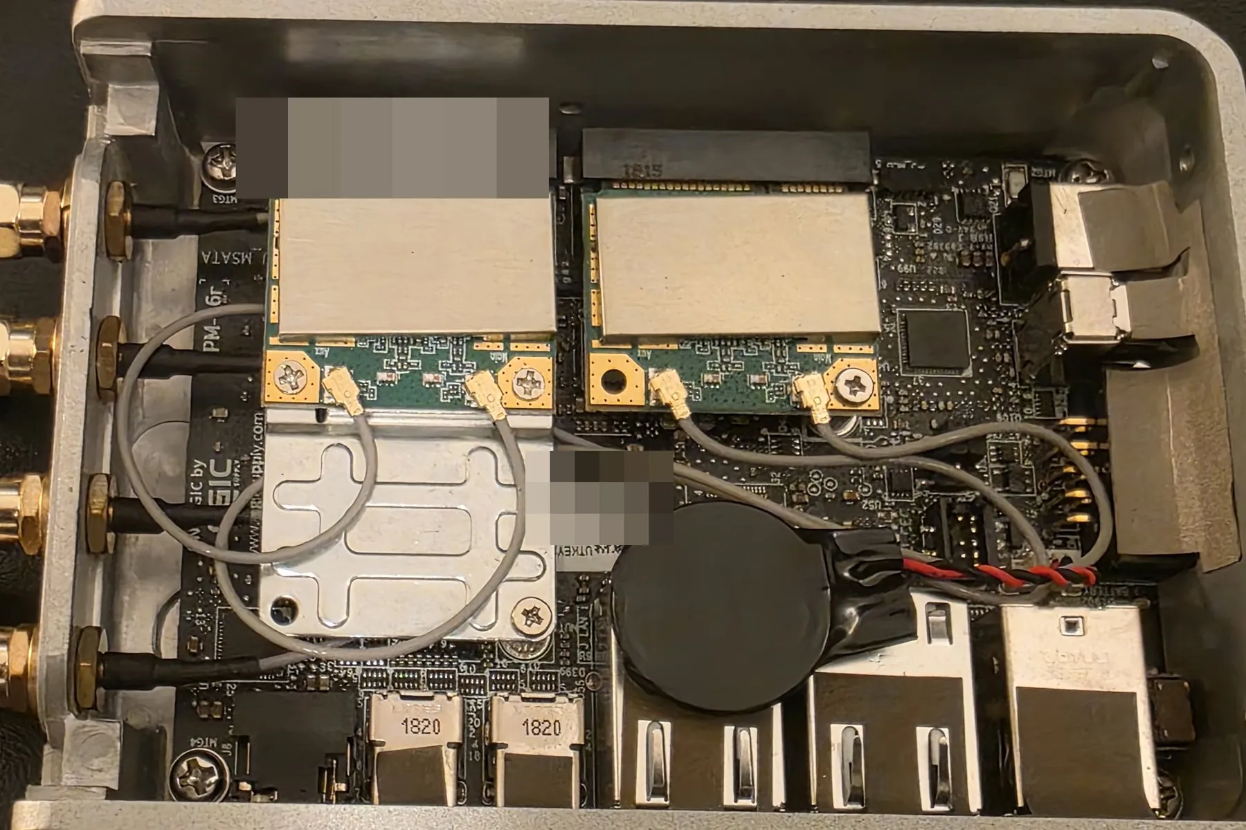 Inside one of the x86 builds: two mini-PCIe radio cards seated side by side, each wired by thin u.FL pigtails that loop across to gold SMA antenna bulkheads on the case wall, next to the coin cell and dual Ethernet magnetics.