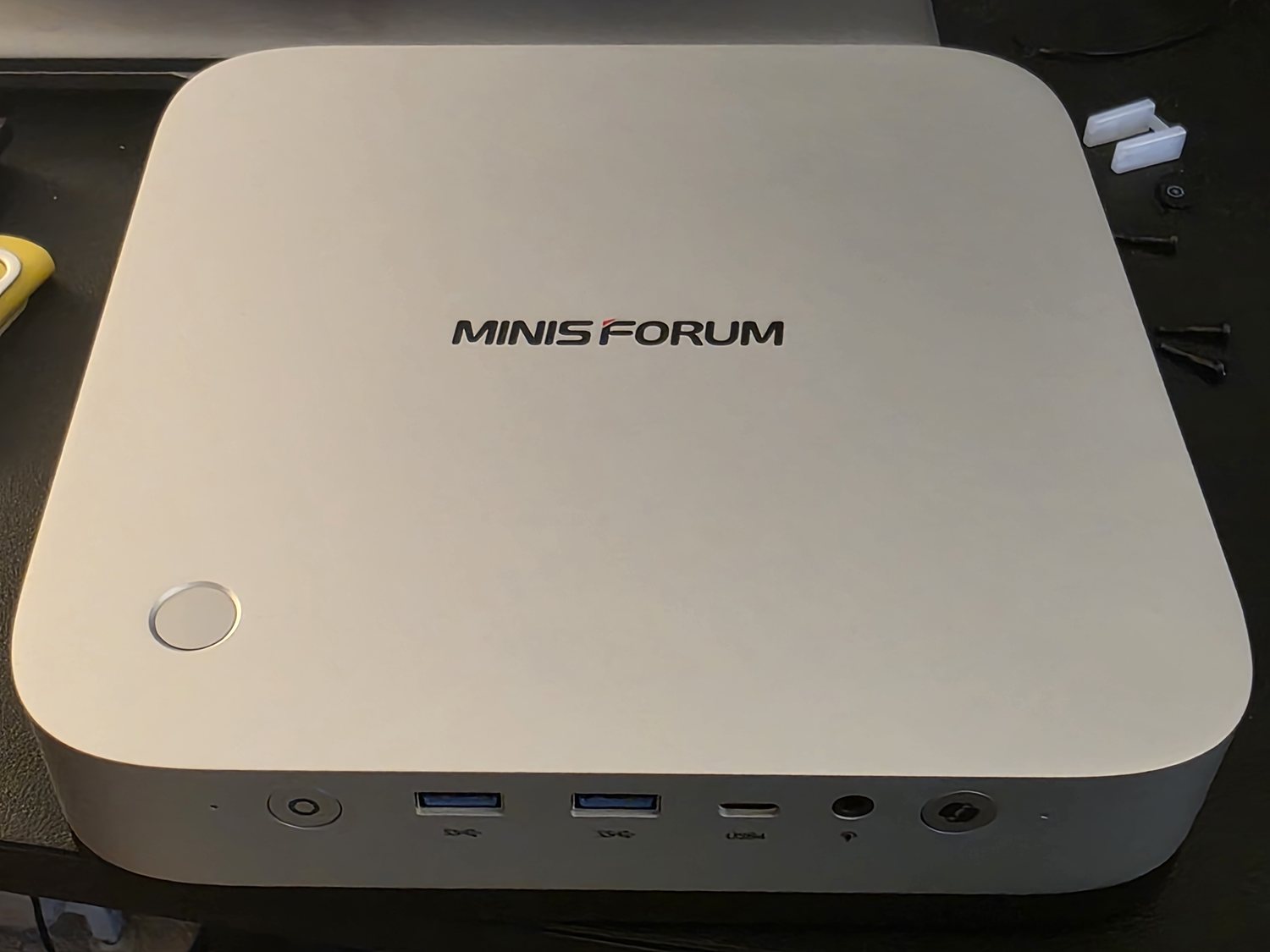 A MINISFORUM AI X1 Pro-470 — a small white mini-PC — sitting on a desk mat with its front USB and USB4 ports visible.